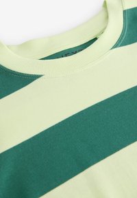 Hanorac cu dungi verzi și galben deschis, cu guler cu margine reiată, având material moale și o textură subtilă. Etichetă de marcă vizibilă în interior.