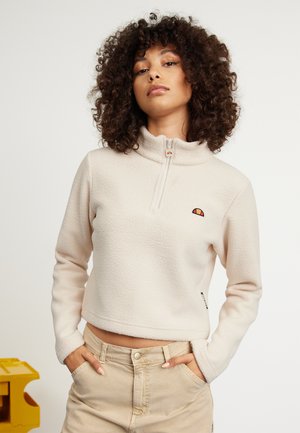 Fleece-neljänesvetoketjupullon vaalea beige, jossa on teksturoitu pinta, ja jonka rinnassa on brodeerattu logo sekä ribattu hihansuudel.