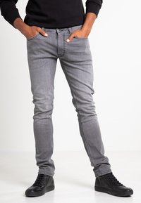Gray denim jeans with a slim fit, five-pocket design, and subtle stitching details. Paired with black high-top sneakers.
