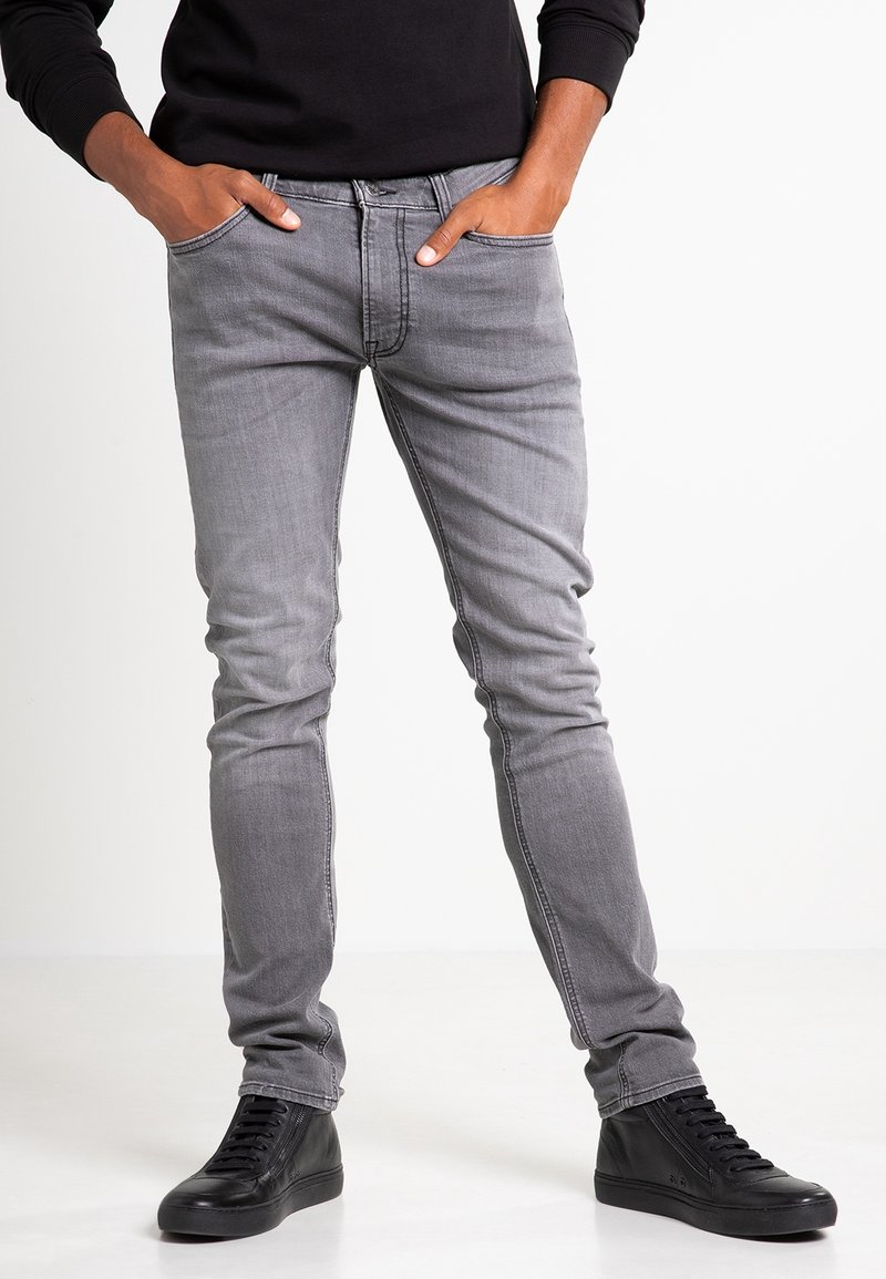Gray denim jeans with a slim fit, five-pocket design, and subtle stitching details. Paired with black high-top sneakers.
