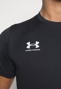 Lähikuvassa henkilö, joka käyttää mustaa Under Armour -T-paitaa, jossa on valkoinen Under Armour -logo ja teksti rinnassa.