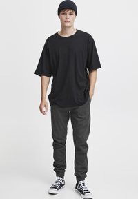 Svart oversized t-skjorte med rund hals, kombinert med mørkegrå joggebukser med elastiske manchetter. Fottøy: svart og hvite sneakers.