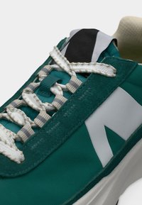 Κοντινό πλάνο αθλητικού παπουτσιού σε τυρκουάζ και λευκό χρώμα με υφή στα λευκά κορδόνια, λεπτομέρειες από σουέτ και παχιά λευκή σόλα.