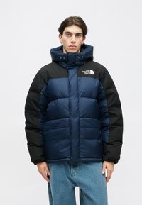 Jakna na napuhavanje u tamnoplavoj i crnoj boji, s podstavom, visokim ovratnikom, kapuljačom s vezicama i logoom na prsima.