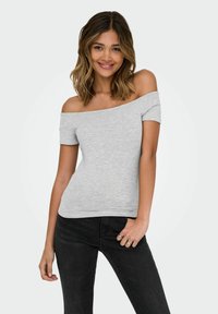 Grå off-shoulder top lavet af blød, letvægtsstof. Har korte ærmer og et tætsiddende design. Navnet det med mørke sorte jeans.