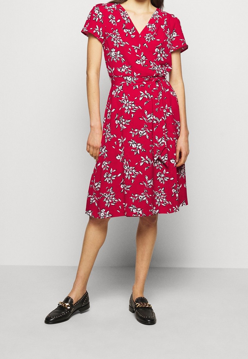 Vestido floral rojo con mangas cortas y escote en V; presenta una cintura ajustada y una falda fluida. Mocasines negros con detalles de cadena dorada.