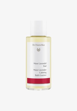 Bouteille en verre transparent avec un capuchon blanc. Le liquide est jaune. L'étiquette affiche "Dr. Hauschka Moor Lavendel Bad" avec un accent rouge et des détails textuels.