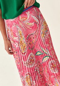 Gonna maxi plissettata di un vivace rosa, con un motivo floreale e paisley, realizzata in tessuto leggero con una consistenza liscia.