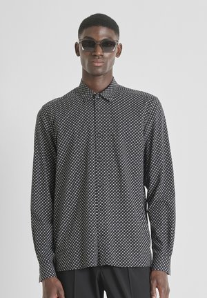 Camicia a maniche lunghe a fantasia bianca e nera con chiusura a bottoni e colletto, indossata con occhiali da sole, su un modello contro uno sfondo neutro.