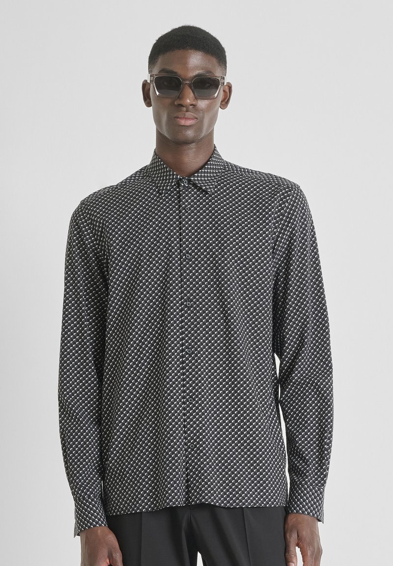 Camicia a maniche lunghe a fantasia bianca e nera con chiusura a bottoni e colletto, indossata con occhiali da sole, su un modello contro uno sfondo neutro.