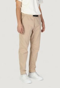 Pantaloni beige elasticizzati con una cintura in vita elastica e cuciture laterali sottili, abbinati a sneakers bianche. Design casual e slim-fit.