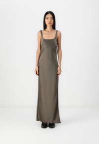 Rochie lungă din satin verde măslin, cu bretele late, decolteu pătrat și siluetă dreaptă, asortată cu încălțăminte neagră.