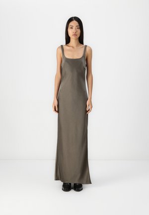 Robe longue en satin vert olive avec de larges bretelles, un décolleté carré et une silhouette droite, assortie à des chaussures noires.
