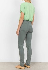 Groen T-shirt met korte mouwen gecombineerd met strakke grijze broeken. De broeken hebben achterzakken en een gladde, licht gestructureerde afwerking.