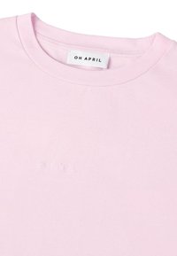 Světle růžové tričko s krátkým rukávem vyrobené z bavlny, s kulatým výstřihem a decentním vyšívaným nápisem "OH APRIL" blízko lemování.
