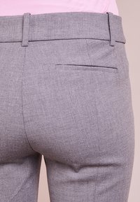 Pantalon gris sur mesure en tissu lisse, avec une taille ajustée et une poche arrière unique au design subtil.