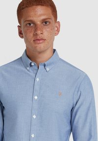 Camicia button-up azzurro chiaro in cotone con colletto, caratterizzata da un piccolo logo ricamato arancione sul petto e bottoni bianchi.
