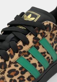 Sneaker con stampa leopardata, strisce verdi, lacci neri e suola in gomma nera a contrasto. Parte superiore testurizzata in materiale morbido.