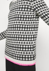 Strickpullover mit schwarz-weißen geometrischen Mustern, mit strukturierter Verarbeitung und pinkem Saum. Klassischer Rundhalsausschnitt; lange Ärmel.