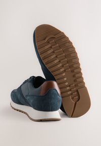 Baskets bleu marine avec une exterior en daim, une garniture en cuir marron, une semelle intermédiaire blanche et une semelle extérieure en caoutchouc texturée. Caractérisées par un bout arrondi et un design à lacets.