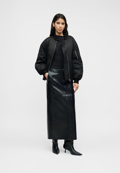 Fekete bomber dzseki steppelt részletekkel, magasderekú fekete bőrszoknyával és hegyes orrú, fekete magassarkú csizmával párosítva.