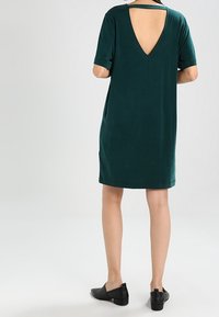 Robe courte à manches courtes de couleur vert foncé, avec un dos en V profond et une texture lisse et douce. Design simple avec une coupe décontractée et longueur au genou.