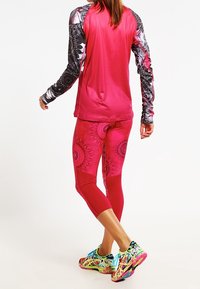 Träningsoutfit som består av en rosa långärmad topp med mönstrade svarta ärmar, matchande rosa leggings och flerfärgade löparskor.