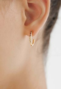 Pendiente de aro dorado con un diseño curvado que presenta piedras preciosas multicolores. Lleva puesto en una oreja, mostrando un acabado pulido y un brillo sutil.