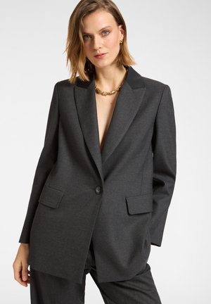 Donkergrijze blazer van een gestructureerde stof, met een reverskraag, een enkele knoopsluiting en voorzakken.