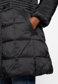 Chaqueta negra acolchada con secciones de acolchado, con cinturilla ajustada, cordón regulable y bolsillos laterales. Textura suave y material resistente a la intemperie.