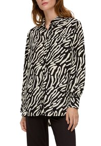 Schwarz-weißes Hemd mit Zebra-Streifenmuster, mit Kragen und langen Ärmeln, aus einem glatten, leichten Stoff gefertigt.