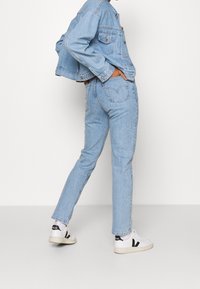 Ljusblå denimjacka med knappstängning och två framfickor, kombinerat med matchande ljusblå jeans och vita sneakers med svarta accenter.