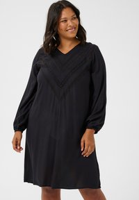 Vestido negro con escote en V y mangas largas abullonadas. Presenta un delicado detalle de encaje en un patrón de chevron en el torso. Textura de tejido suave.