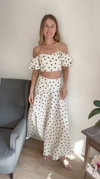 Conjunto de duas peças com bolinhas brancas, apresentando um top ajustado sem alças com babados e uma saia longa e fluida com uma fenda lateral.