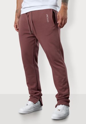 Burgunderfarbene Jogginghose aus weichem Material, mit elastischem Bund und Kordelzug, Seitentaschen und Reißverschluss am Saum. Markenlogo sichtbar.