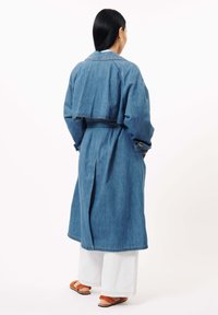 Denim trenchcoat met een cropped bovenlaag, lange mouwen en een verstelbare riem. Bevat een ventileeropening aan de achterkant en heeft een comfortabele pasvorm. Gecombineerd met wijde broekspijpen.