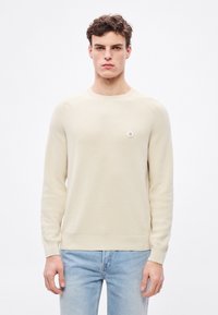 Svetloružový pletený sveter s dlhými rukávmi, okrúhlym výstrihom a rebrovanými manžetami. Na ľavej strane hrudníka sa nachádza malé okrúhle logo.