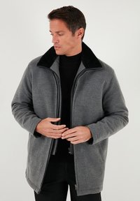 Abrigo de forro polar gris con cuello negro, cierre frontal con cremallera, mangas largas y bolsillos laterales. La tela parece suave con una textura lisa.