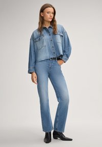 Light blue denim shirt with cropped design, two chest pockets, and black buttons; paired with matching light blue jeans and black ankle boots.