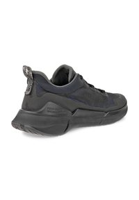 Black athletic shoe with mesh fabric upper, rubber sole, and a patterned heel loop. Features a sleek design and textured surface.