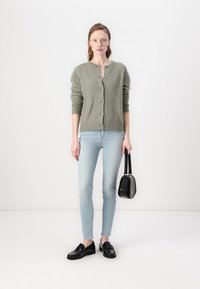 Light green, button-up cardigan made of soft knit fabric, paired with light blue skinny jeans, black loafers, and a small black handbag.
