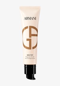 Beige rör med en svart pump, har "Armani"-logotypen och "Giorgio Armani"-emblemet i brunt. Texten lyder "Skin Tint long-wear & care."