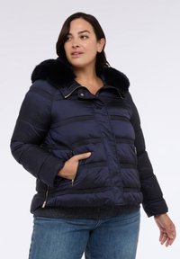 Marineblaue Steppjacke mit Kunstfellkragen, horizontalen Nähten, Reißverschlusstaschen und goldenem Beschlag, mit einer warmen, glatten Außenseite.