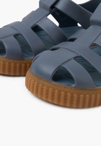 Gray plastic sandals with a strappy design and a textured brown rubber sole. Features open toes and sides for breathability.