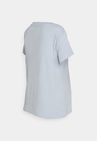 Camisa de manga curta azul clara em textura canelada, com um decote redondo e detalhe de etiqueta lateral, apresentando um design limpo e simples.