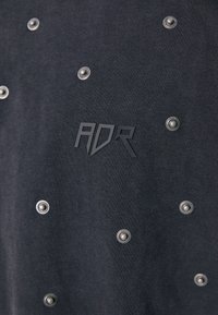 Mustakirjude ja reljeefse "ADR" logo külge õmmeldud must puuvillane riietus. Kangas on sileda tekstuuriga ja nähtavate õmblusdetailidega.