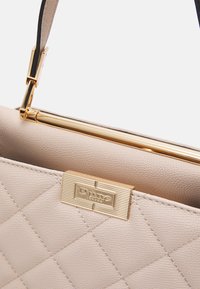 Beige quiltet håndtaske med gyldent spænde og logo. Har en glat tekstur og et struktureret design med en aftagelig rem.