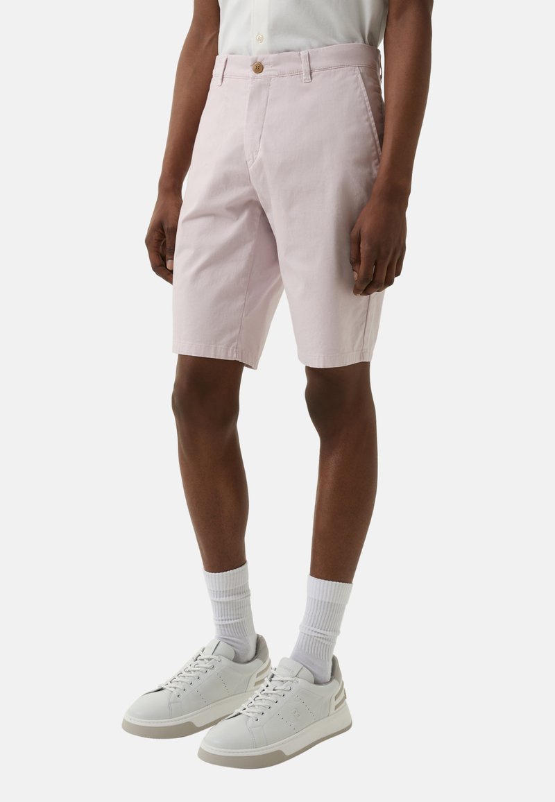 Helle rosa Baumwoll-Shorts mit einem geknöpften Bund und frontalen Taschen. Kombiniert mit weißen Sneakers und gerippten weißen Socken.