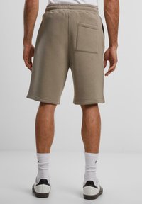 Khaki bomullsshorts med elastisk midje, med en baklomme og synlig søm. Midt på låret lengde med en myk tekstur.