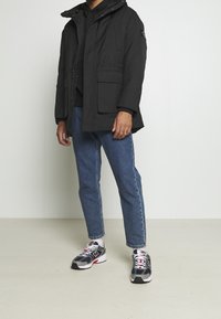 Czarna parka z kapturem i przednimi kieszeniami, nałożona na czarną bluzę z kapturem. W połączeniu z jasnoniebieskimi dżinsami i szarymi trampkami z czerwonymi akcentami.